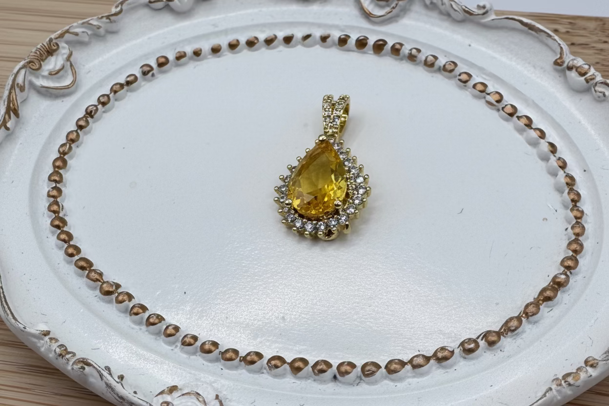 Gold pendant with a yellow teardrop-shaped gemstone on a decorative white plate.