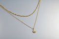 Gold chain necklace with a sun pendant on a red background